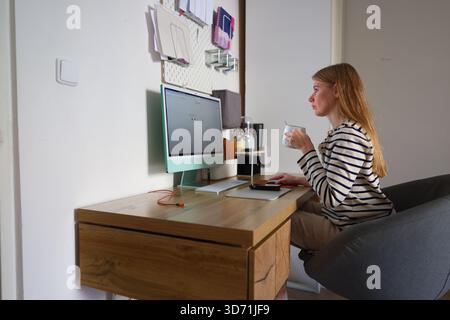 Konzept der Fernarbeit, Frau, die den Computer am modernen Holztisch mit Kaffeetasse benutzt. Stockfoto