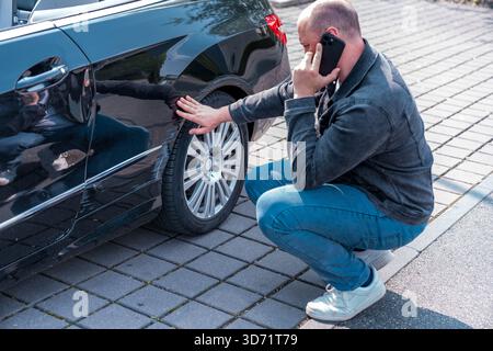Mann, der ein verkratztes Auto inspiziert und die Versicherung anruft, nachdem das Fahrzeug beschädigt wurde Stockfoto