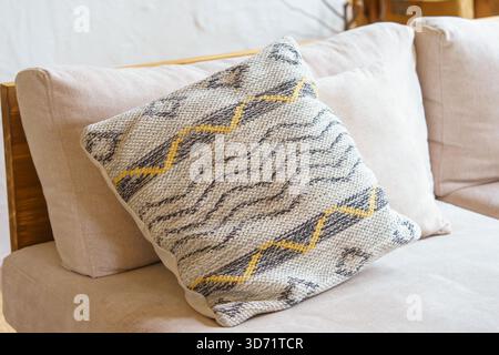 Weiches Dekokissen, Kissen mit geometrischer Webstruktur und gelbem Zickzackmuster auf hellbeigem Sofa. Gemütliches, minimalistisches skandinavisches Interieur mit Stockfoto