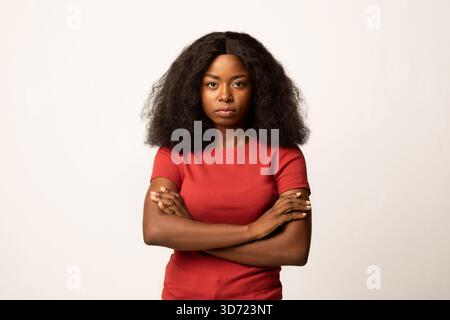 Selbstbewusste junge afroamerikanische Frau mit überkreuzten Armen im Studio-Setting Stockfoto