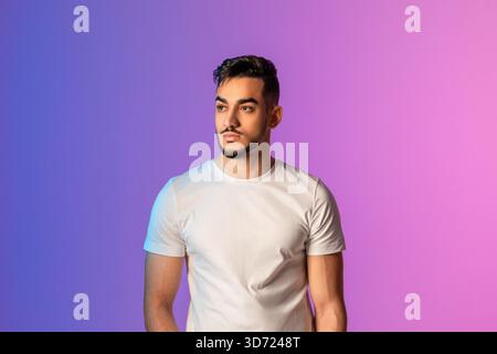 Ernster junger arabischer Mann posiert in weißem T-Shirt unter leuchtendem Neonlicht Stockfoto