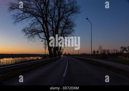 Stadtstraße und Bürgersteig bei Sonnenuntergang. Dramatische Himmelslandschaft im November in Lettland Stockfoto