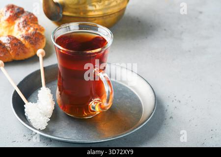 Türkischer schwarzer Tee. Eine Glasschale türkischer schwarzer Tee und knuspriger türkischer traditioneller Bagel auf grauem Betontischhintergrund. Frühstücksgebäck-Konzept. Traditionelles türkisches Heißgetränk. Stockfoto