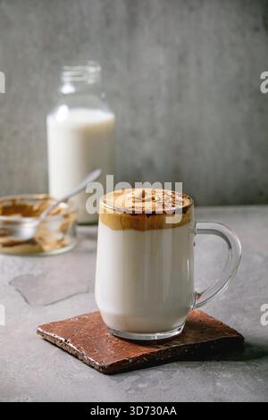Dalgona schäumender Kaffee Trend koreanischer Drink Milchlatte mit Kaffeeschaum in Glasbecher, dekoriert mit gemahlenem Kaffee auf grauem Texturtisch. Zutaten oben. Kopierbereich Stockfoto