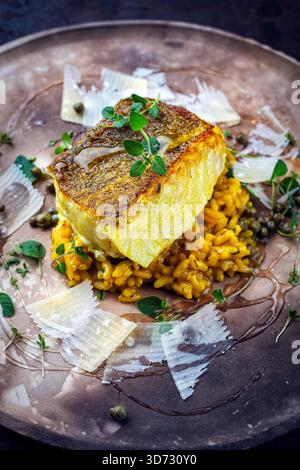 Gebratenes Fischfilet aus nordischem Kabeljau mit safran-Risottoreis, grünem Gemüse und Parmesankäse Stockfoto