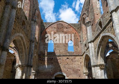 Innere Ruinen der Zisterzienserabbazia di San Galgano aus dem 13. Jahrhundert in der Nähe von Chiusdino mit gotischen Steinbögen und überdachlosen Ziegelmauern. Stockfoto