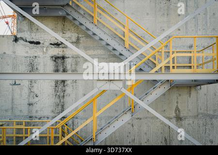 Eine detaillierte Ansicht einer Industrietreppe mit gelben Geländern, Stahlquerverstrebungen und einer Betonwand, die die Bautechnik und die DE hervorhebt Stockfoto