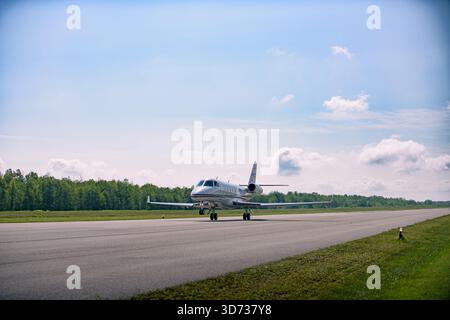 Ein kleiner Privatjet auf der Startrolle mit Nasenrad, das von der Start- und Landebahn abhebt, Weitwinkel-Vorderansicht bei hellem Tageslicht mit Bäumen und weichem Himmel Stockfoto