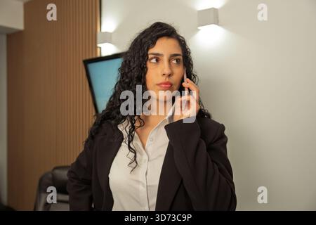 Geschäftsfrau, die mit dem Smartphone spricht und in einem professionellen Büroumfeld ernsthaft aussieht Stockfoto