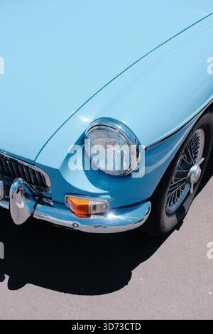Nahaufnahme der vorderen Ecke eines hellblauen Oldtimers mit rundem Scheinwerfer, Chrom-Stoßfänger, Kontrollleuchte und klassischem Drahtrad. Stockfoto