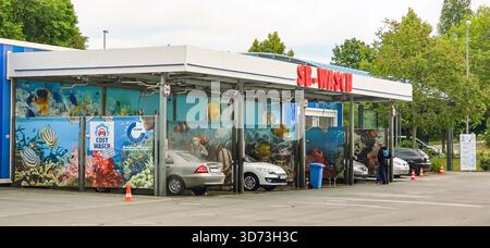 Berlin, Deutschland - 18. Mai 2025: Die Waschanlage zeigt ein farbenfrohes Unterwasserbild mit geparkten Fahrzeugen und Kunden in der Nähe. Stockfoto