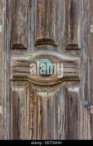 Rustikale verwitterte Holztür mit grünem Metallknopf und Rissverzierung Stockfoto