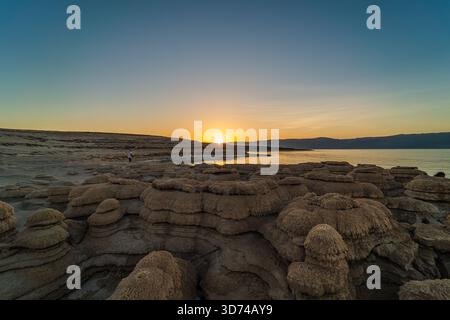 Salzpilzartige Formationen am Toten Meer bei Sonnenaufgang, warmes goldenes Licht, das weiße Mineralkappen über ruhigem türkisfarbenem Wasser beleuchtet. Stockfoto
