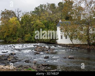 Ein großer Blick auf ein weißes historisches Mühlengebäude neben dem Brandywine Creek mit rauschenden Stromschnellen und Felsen im Vordergrund. Stockfoto