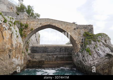 Ein junges Paar auf der mittelalterlichen Brücke in Castro Urdiales, Kantabrien, Spanien. Das malerische Dorf liegt entlang der Route des Camino del Norte des Weges Stockfoto