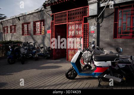 Motorroller standen vor einer verzierten roten Tür in einem ruhigen Pekinger Hutong Stockfoto