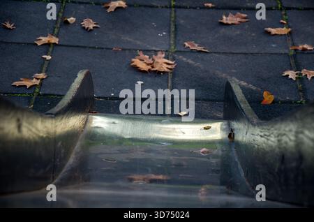 Herbstlaub auf leerem Spielplatz Rutsche und Gummiboden Stockfoto
