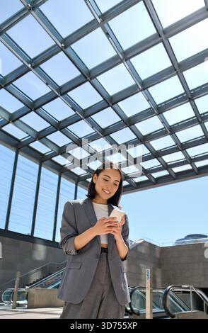 Lächelnde junge asiatische Geschäftsfrau, die mit dem Telefon in der U-Bahn der Stadt steht Stockfoto