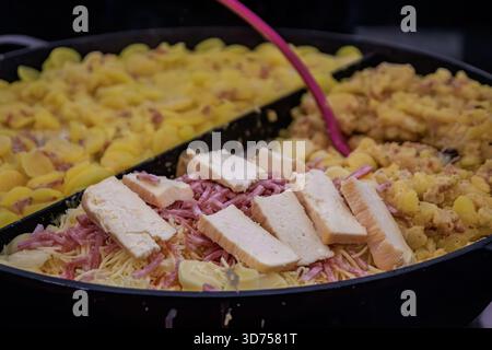 Traditionelle elsässische Tartellette mit Reblochon-Käse, Speck, Zwiebeln und Kartoffeln in einer großen Pfanne auf dem Weihnachtsmarkt in Straßburg, Frankreich Stockfoto