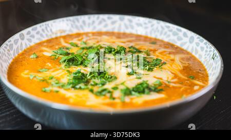Herzhafte Fleisch- und Gemüsesuppe mit frischer Petersilie und geschmolzenem Käse, serviert in einer rustikalen Schüssel. Angenehm, geschmackvoll und perfekt für kalte Tage. Stockfoto
