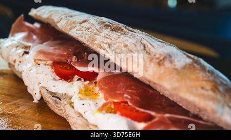 Italienisches Baguette mit cremiger Burrata, Schinken, Kirschtomaten, Olivenöl und Kräutern. Ein einfaches, elegantes, italienisch inspiriertes Mittagessen oder Vorspeise, frisch Stockfoto