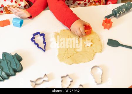 Zwei Kinder machen zu Hause eine Feiertagsbacken-Aktivität, indem sie mit bunten Ausstechern aus Teig Formen schneiden. Die Szene ist fröhlich, gefüllt mit f Stockfoto