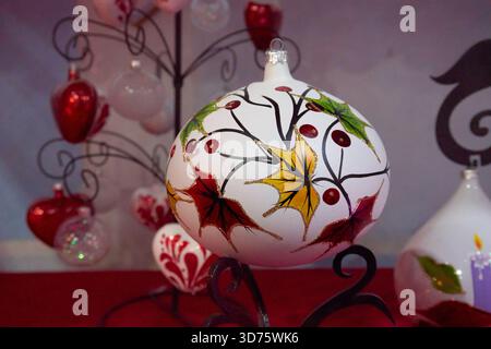 Eine weiße Vase mit gemalten Blättern steht auf einem Tisch. Die Vase ist von anderen Vasen umgeben, von denen einige rot sind. Mexiko, Puebla, Chignahuapan, DE Stockfoto
