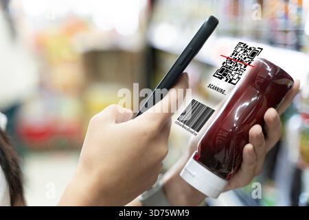 Smartphone scannt den QR-Code und den Barcode eines Produkts in einem Supermarktgang und repräsentiert digitalen Informationszugriff, intelligentes Einkaufsverhalten, Einzelhandel Stockfoto