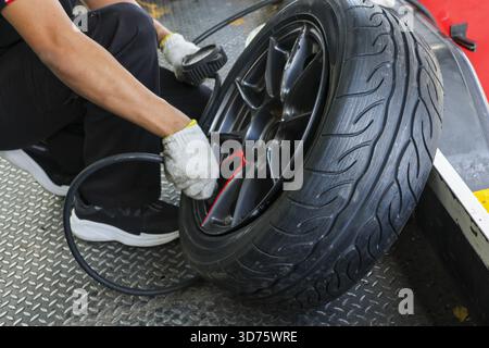 Fokussierter Mechaniker, der Autoreifen auf einer Leichtmetallfelge in der Garage aufpumpt. Der professionelle Service bietet Wartung und Reparatur und überprüft den Luftdruck auf Sicherheit Stockfoto