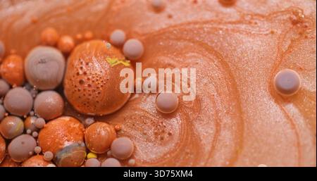 Verschütteter Hintergrund. Farbtropfen. Unschärfe orange lila gelbe Farbblasen flüssiges Spargel Öl Glitzer Pigment schwimmend auf Acrylabstraktion. Stockfoto