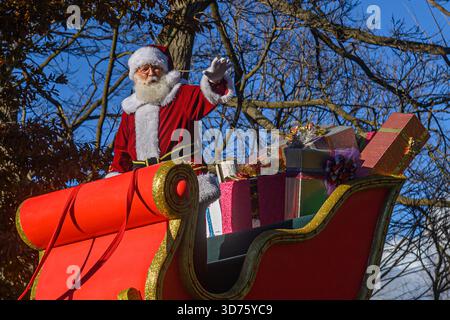 TORONTO, ONTARIO, KANADA - 23. NOVEMBER 2025: Der Weihnachtsmann winkt der Menge, während er in seinem legendären rot-goldenen Schlitten fährt, der mit einem g-gewickelten Haufen hoch gestapelt ist Stockfoto