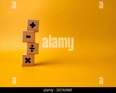 Das Bild zeigt vier Holzblöcke mit grundlegenden mathematischen Betriebssymbolen auf gelbem Hintergrund. Stockfoto