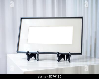 Leeres Panoramafoto oder Mockup in elegantem schwarzem Rahmen mit mattem und Displayständer auf weißem Tisch, perfekt für horizontale Ausdrucke, c Stockfoto