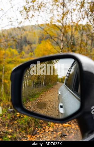 Talas, Kasachstan - 13. Mai 2024: Eine malerische Herbstwaldstraße mit gelbem Laub, die sich im Seitenspiegel eines silbernen Toyota Land Cruiser 300, su, spiegelt Stockfoto
