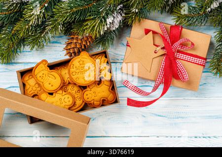 Lebkuchenkekse, Geschenkbox und verschneite Tannenzweige auf hölzernem Hintergrund Stockfoto