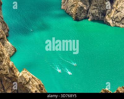 Extrem hohe Winkel aus der Nähe von drei kleinen Schnellbooten, die auf dem lebendigen, kristallklaren türkisfarbenen Wasser eines Bergsees erwachen Stockfoto