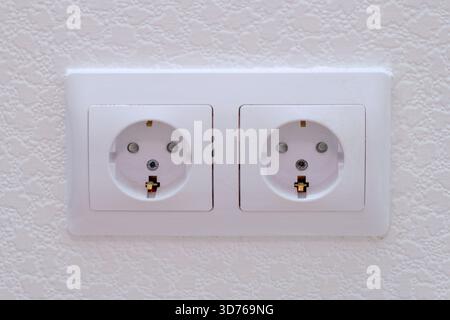 Weiße Wandsteckdose mit zwei Steckdosen an einer strukturierten Wand. Elektrischer Stromanschluss für die Sicherheit zu Hause und im Büro. Stockfoto
