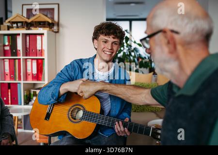 Eine Gruppe älterer Menschen singt zusammen mit jungen Freiwilligen, die Gitarre spielen. Stockfoto