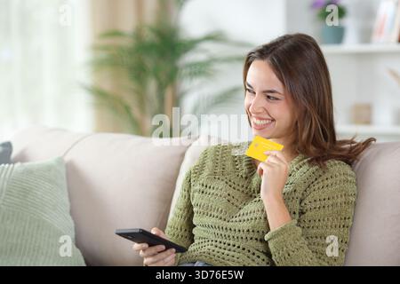 Glückliche Frau in grünem Denken und online kaufen mit Kreditkarte und Telefon auf einem Sofa zu Hause Stockfoto