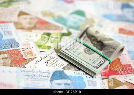 Ein Haufen US-Dollar-Scheine liegt auf einer großen Menge pakistanischer Rupien-Banknoten aus nächster Nähe. Amerikanisches Geld lügt auf Pakistans Geldrechnungen. Das Konzept der Ökonomie und des Devisenaustausches in Pakistan Stockfoto