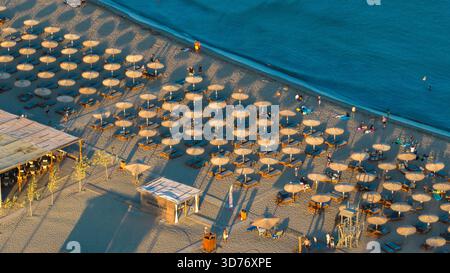 Aus der Vogelperspektive sehen Sonnenschirme, die Schatten am Ufer werfen, im Kontrast zum türkisfarbenen Meer, Kolympia, Rodos, Griechenland. Stockfoto
