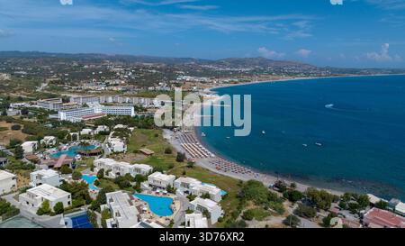 Aus der Vogelperspektive auf den sonnenverwöhnten Strand trifft auf das azurblaue Meer, gesäumt von weißen Gebäuden und einer Vielzahl von Booten, Kolympia, Rodos, Griechenland. Stockfoto