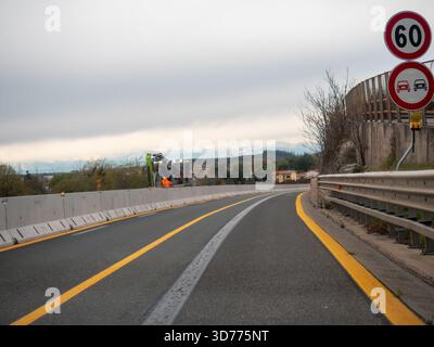 Friaul, Italien 21. November 2025 kurvige A4-Autobahn mit Straßenbau mit Bagger, Sicherheitsbarrieren und Geschwindigkeitsbegrenzungsschildern unter bewölktem Himmel Stockfoto