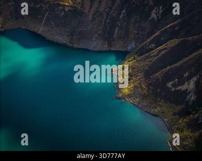 Aus der Vogelperspektive auf das türkisfarbene Wasser treffen auf die zerklüfteten, sonnendurchfluteten Klippen des Quilotoa-Sees in der Provinz Cotopaxi, Ecuador. Stockfoto