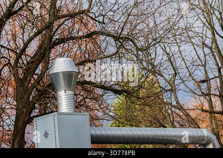 Ein silberner Schornstein erhebt sich deutlich vor einem grauen Himmel, umgeben von blattlosen Bäumen. Stockfoto