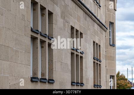 Ein Steingebäude hat eine strukturierte Fassade mit mehreren quadratischen Fenstern. Der bewölkte Himmel bildet eine dramatische Kulisse und trägt zum Archit des Gebäudes bei Stockfoto