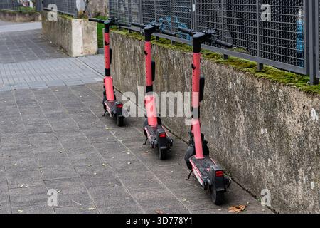 Drei rosafarbene Elektroroller stehen neben einer Betonmauer in einer Stadt. Die Roller stehen ordentlich auf einem Bürgersteig und bieten einen einfachen Modus o Stockfoto