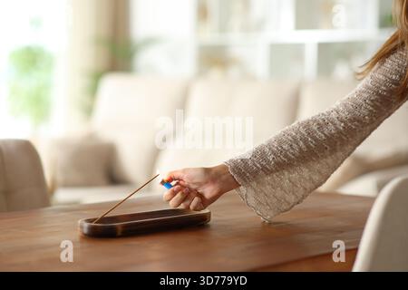 Nahaufnahme einer Frau, die Weihrauchstäbchen auf einem Holztisch im Wohnzimmer zu Hause anzündet Stockfoto