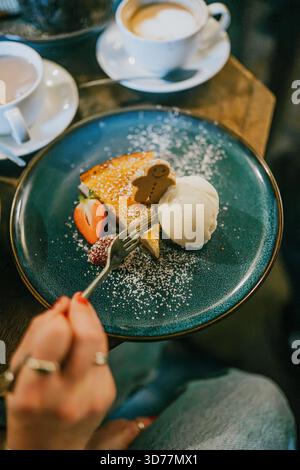 Eine Person isst ein Dessert mit einer Gabel. Das Dessert wird mit Schlagsahne und Erdbeeren garniert Stockfoto