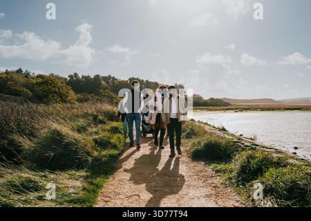 Eine Gruppe von Menschen läuft auf einem Pfad in der Nähe eines Gewässers. Die Szene ist friedlich und ruhig, während die Gruppe einen gemütlichen Spaziergang in der Natur genießt Stockfoto